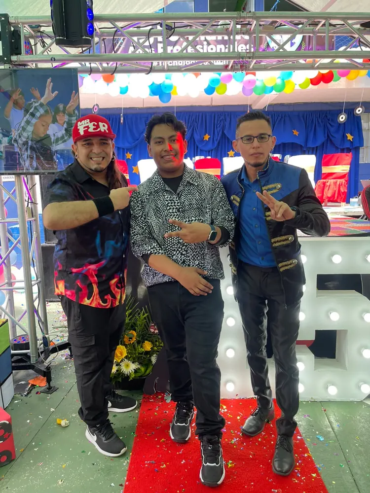 Tres invitados posan en la alfombra roja del evento, con globos y luces al fondo