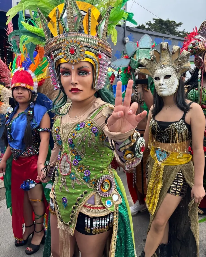 Estudiante con un elaborado traje verde y dorado y un tocado de plumas durante el desfile